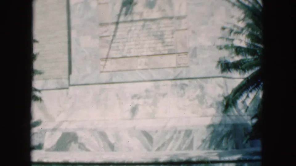 1975 Florida 8mm frame with a soft close view of the stone monument surface, carved panel edge, inscription area, palm fronds, and gate borders.