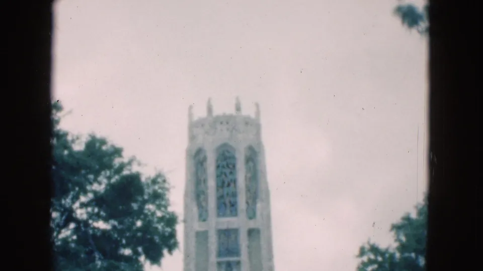 1975 Florida 8mm frame showing a tall Gothic-style tower with arched window openings framed by trees and cloudy sky.