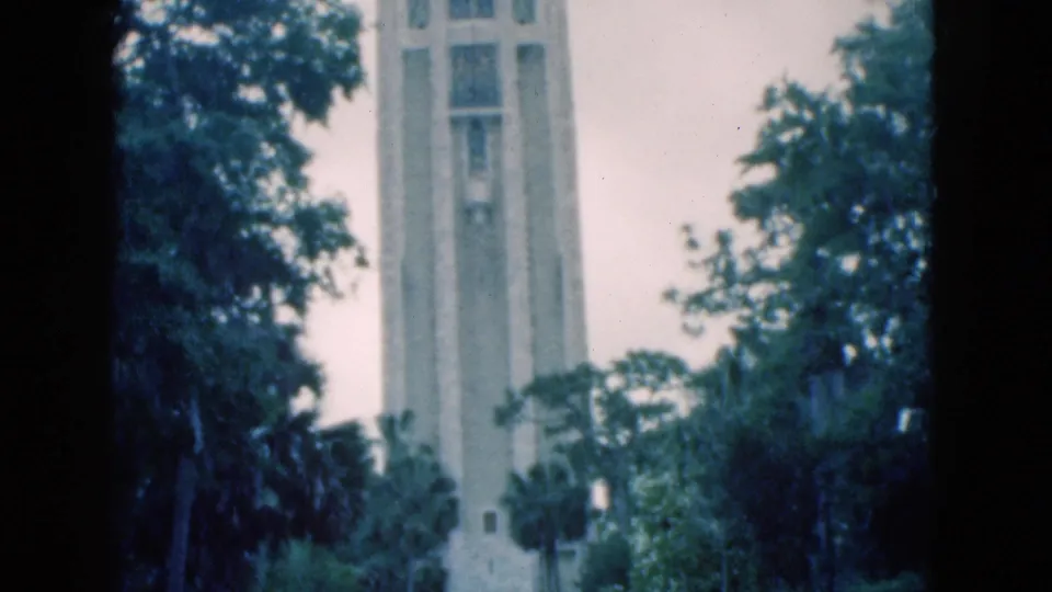 1975 Florida home-movie view of the pale tower framed by dense foliage and a central dark film edge.