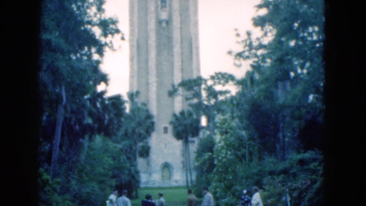 Visitors stand in a lush park before a tall pale stone tower.