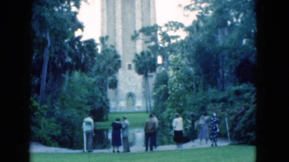1975 Florida park view with visitors spaced along the walkway, dense vegetation, and the pale tower partly framed by trees.