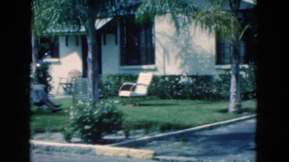 At the end of the clip, the woman is partly cropped at left while the Florida yard, palms, chairs, and house remain in view.
