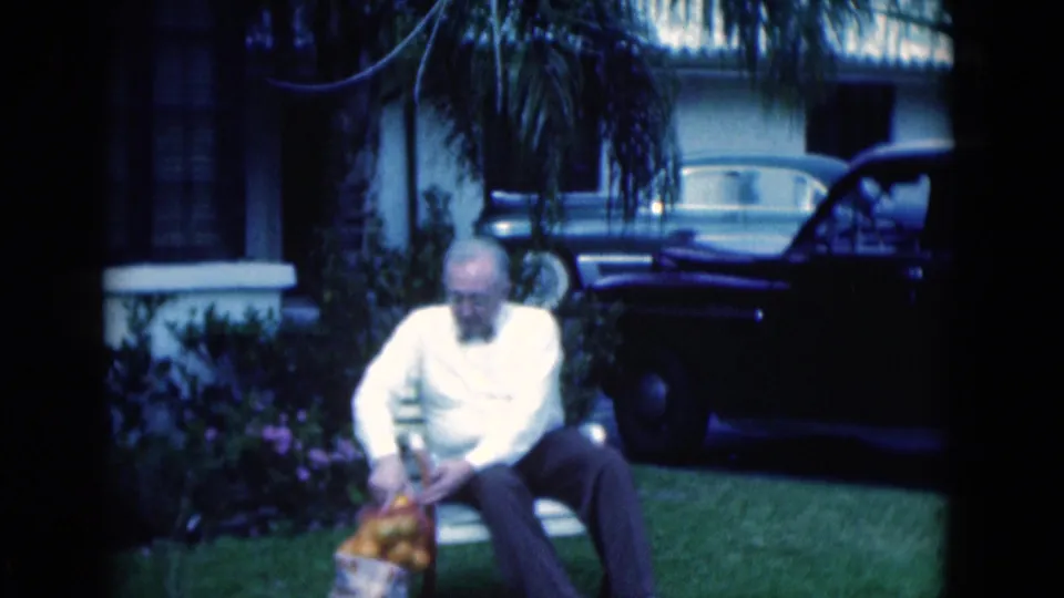 A seated older man looks down toward oranges in a Florida residential yard, framed by 8mm film borders.