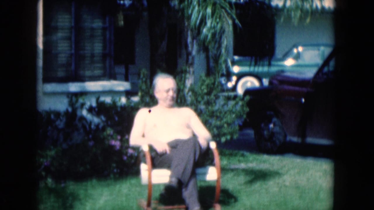 Seated elderly man on a lawn with a small dark butterfly visible near his upper chest.