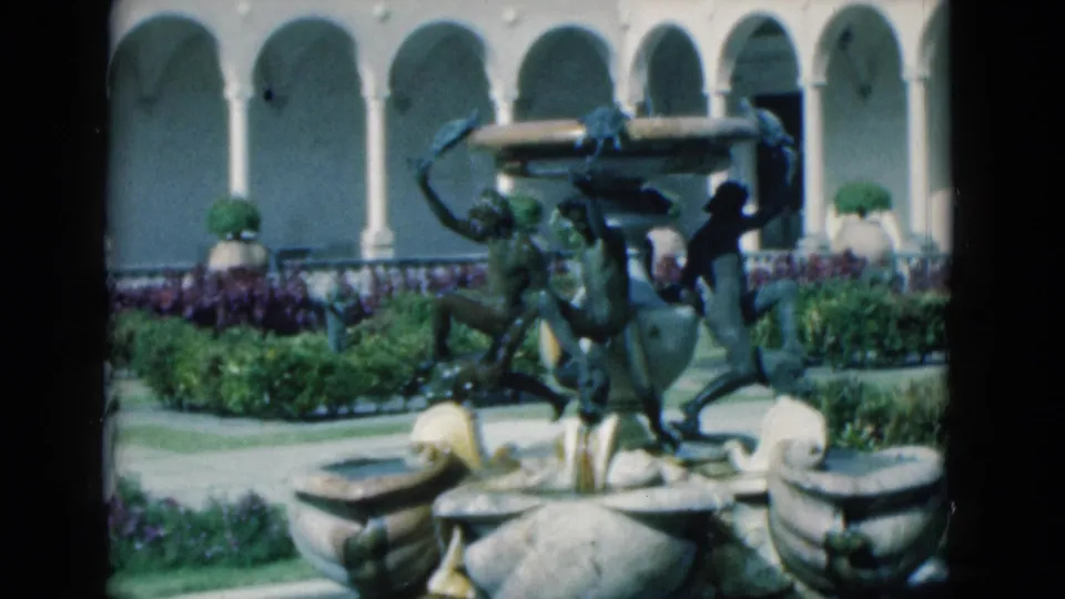 The 8mm frame centers the ornate fountain and courtyard plantings, with the woman partly visible at the side of the garden scene.