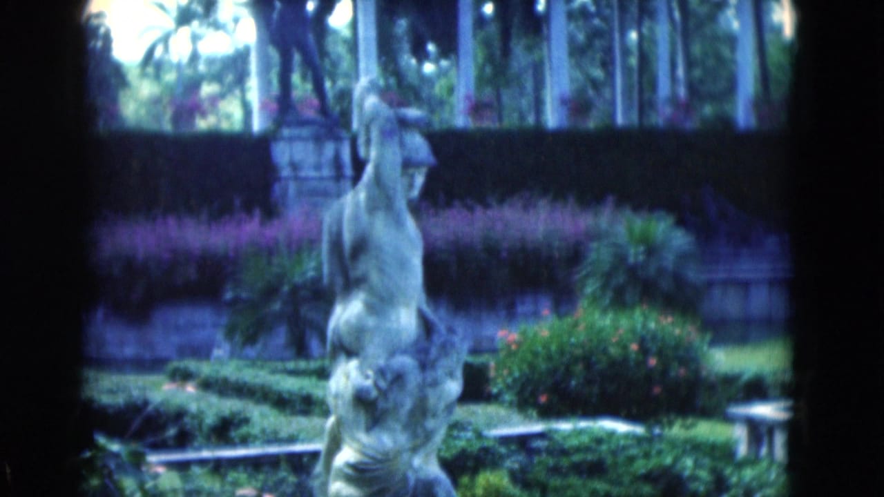Classical garden statue before hedges and palm trees.