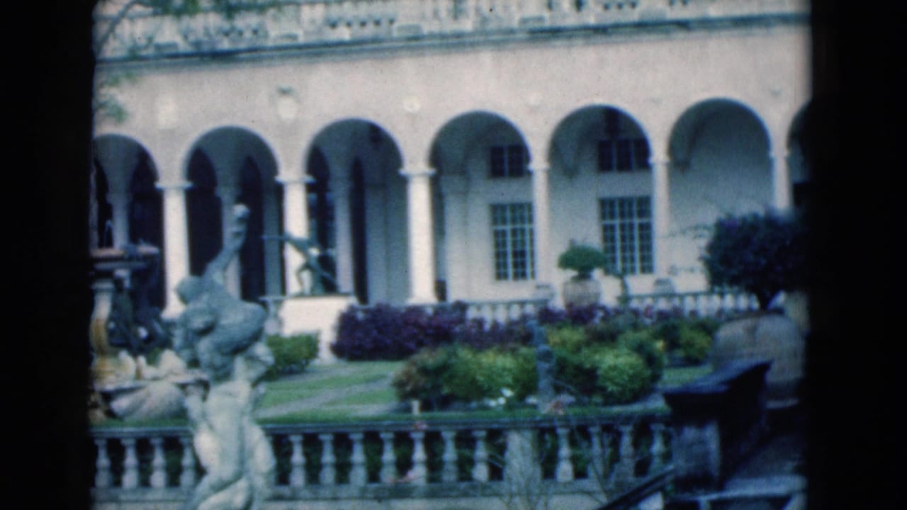 Arched courtyard facade with stone railing, garden plantings, and classical statues.