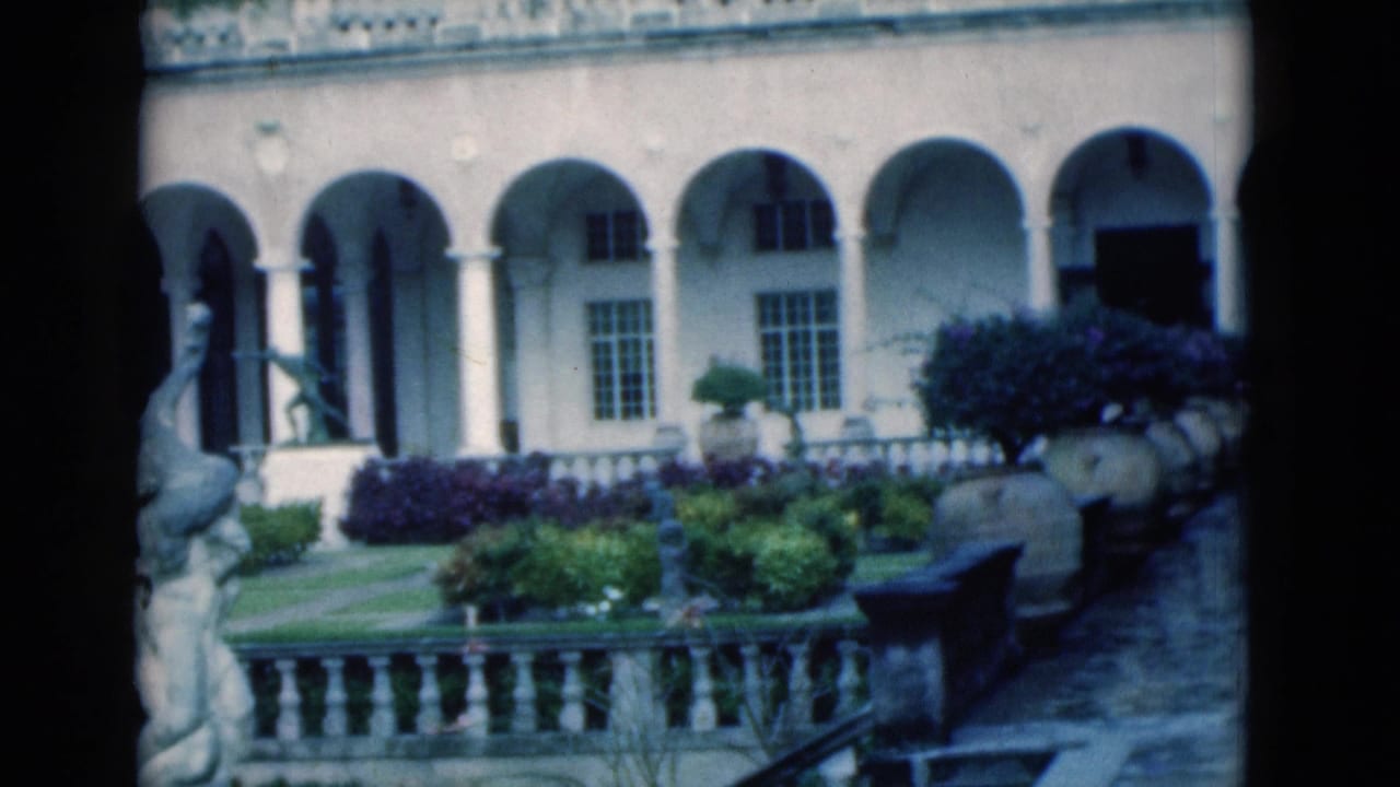 Courtyard garden with arched facade, stone railing, shrubs, and a bench-like seat.