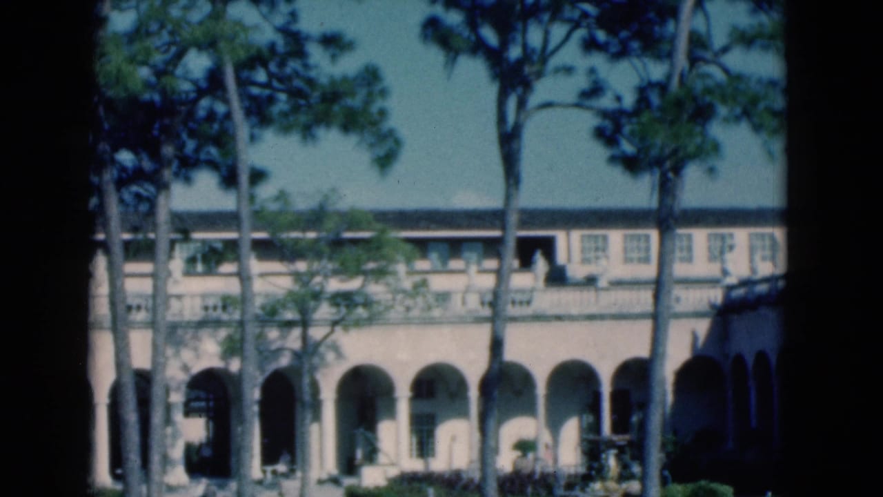 Long arched facade with pine trees and garden details in front.