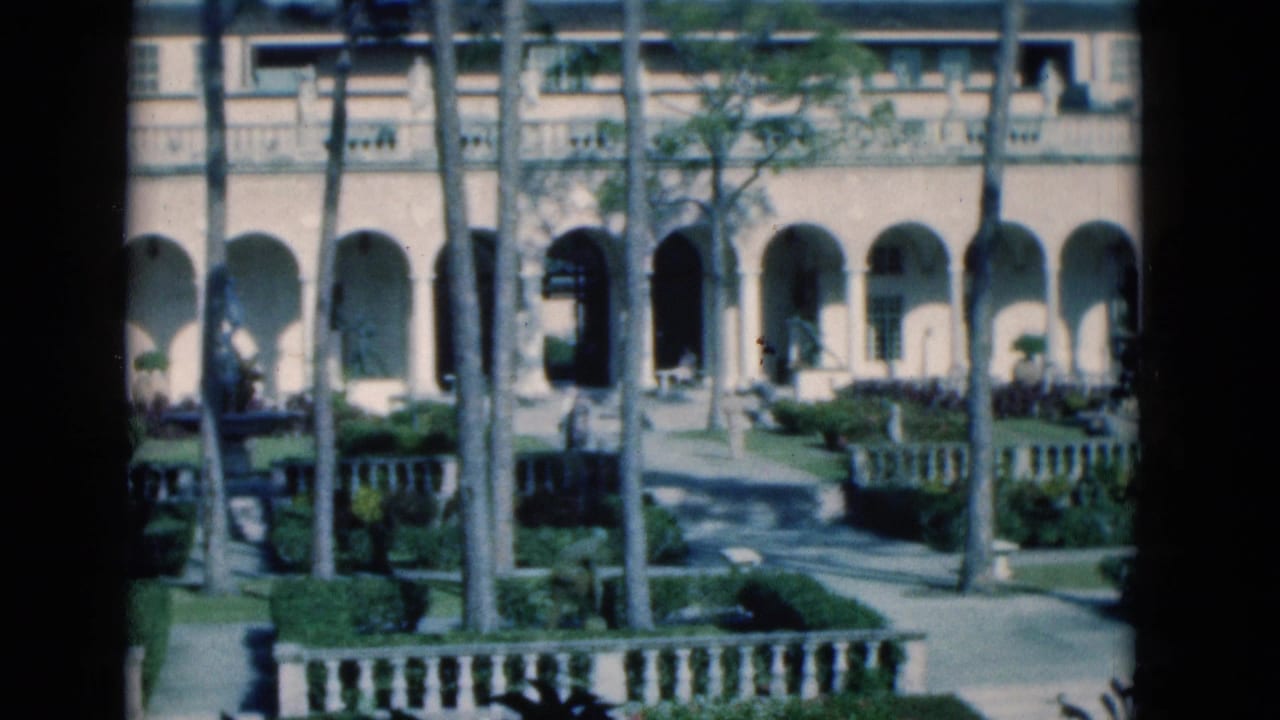 Courtyard with arched colonnades, palm trees, hedges, paths, and a stone balustrade.