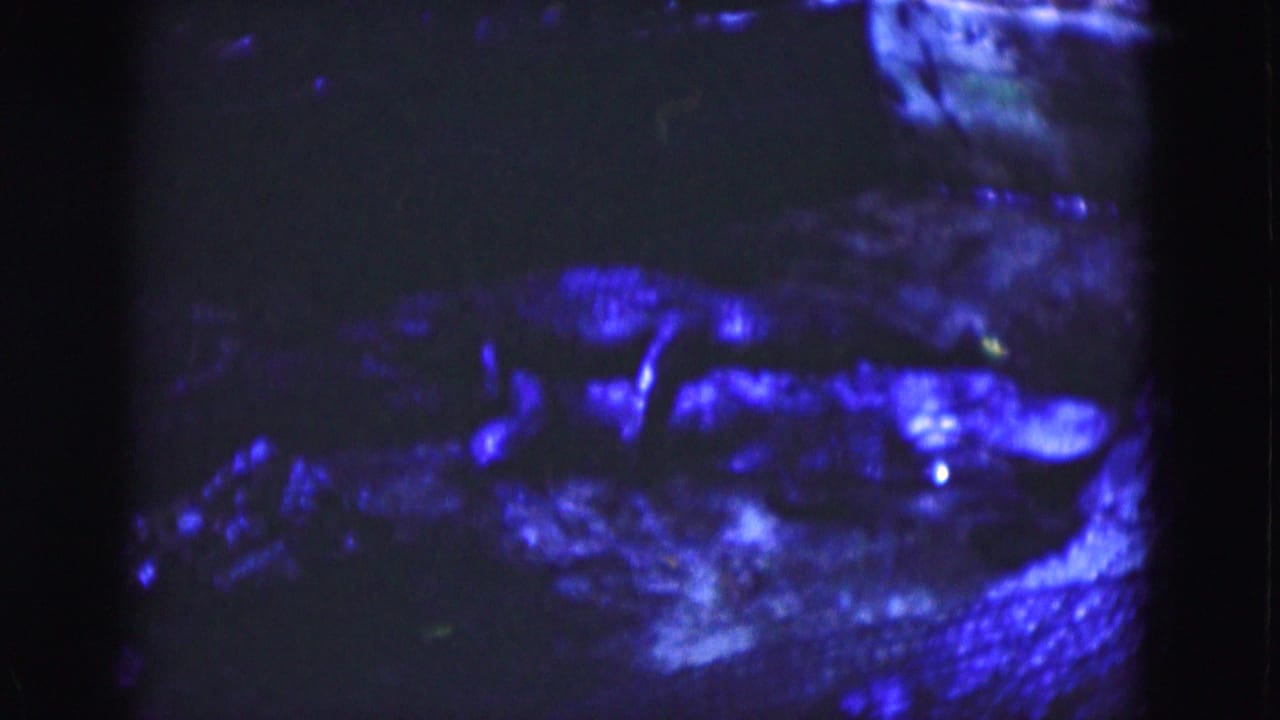 1975 Florida 8mm frame with saturated blue light on unclear rough surfaces, deep shadow, grain, and soft focus.