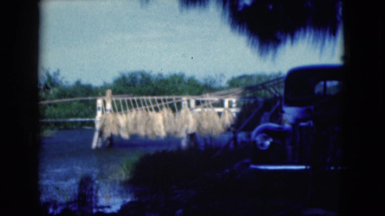 Wooden roadside structure with drying crops and a dark vintage car at the right edge.