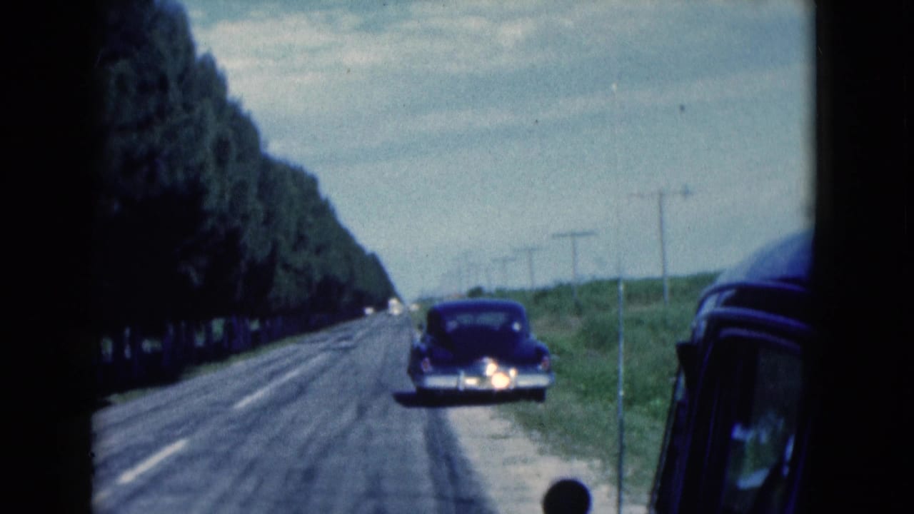 Parked dark sedan on the roadside beside a straight road with trees and utility poles.