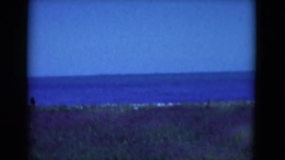 A handheld 8mm view of the Florida coast shows blue sea, pale sky, and grassy foreground with heavy film-frame edges.
