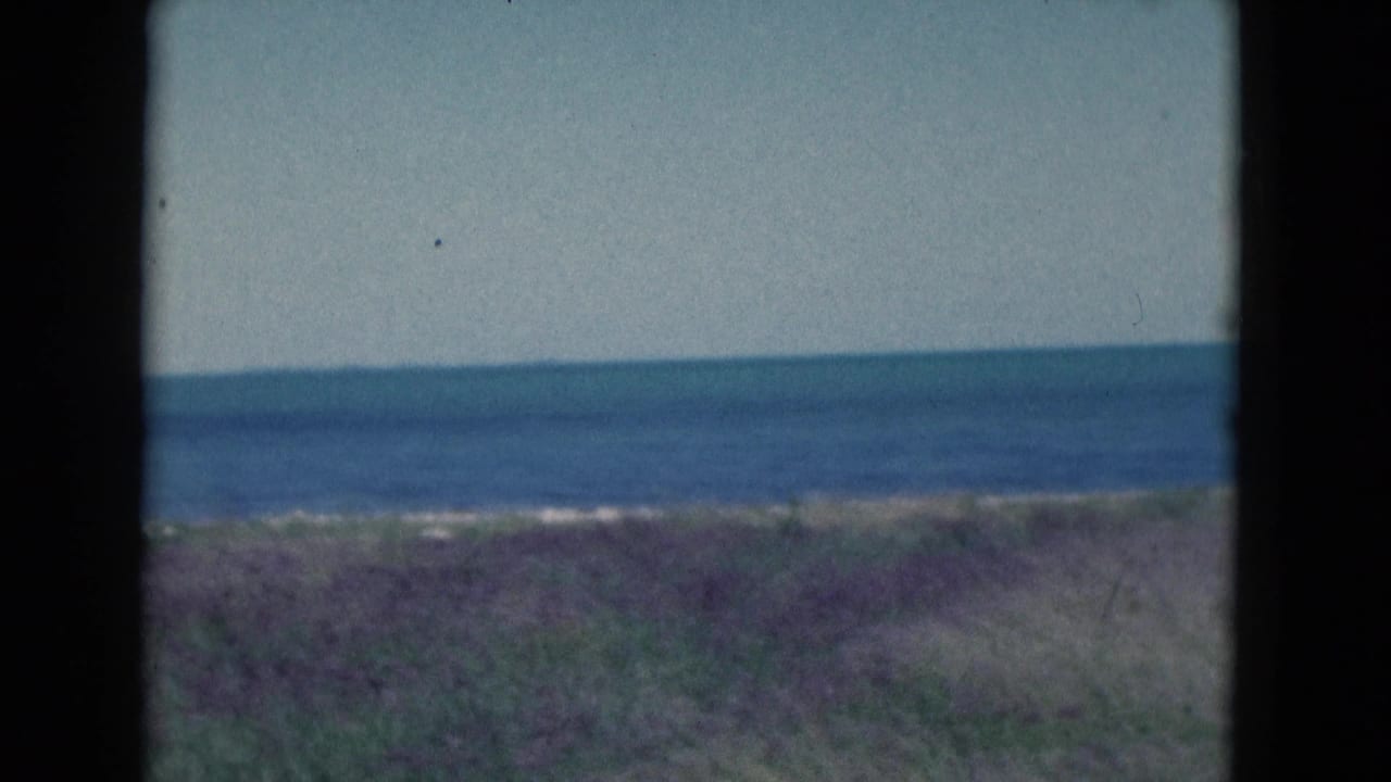 1975 Florida coastal view on 8mm film, with blue water, low dunes, and a quiet open horizon.
