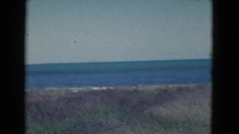 1975 Florida coastal view on 8mm film, with blue water, low dunes, and a quiet open horizon.