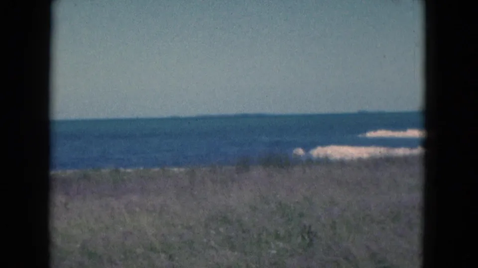 End frame of the 1975 Florida beach pan, showing low dunes, ocean, and small white surf along the shore.