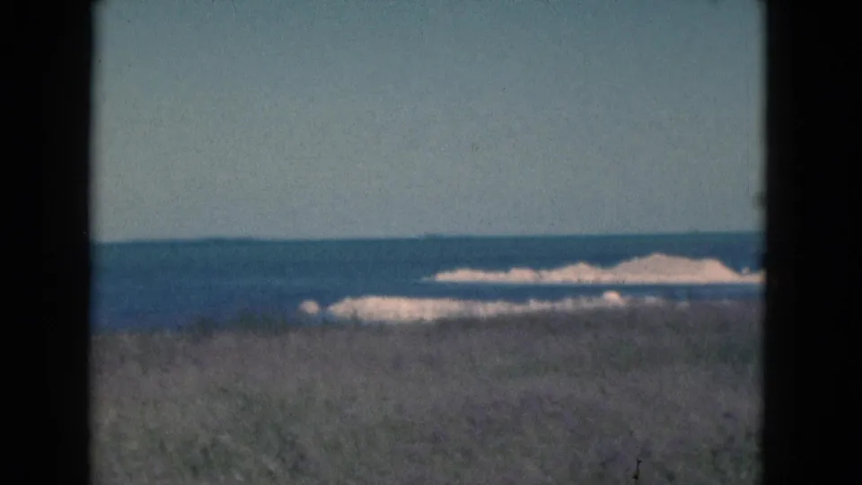 1975 Florida coastal frame showing a blurred grass foreground, open ocean, pale surf, and clear sky within visible 8mm gate edges.
