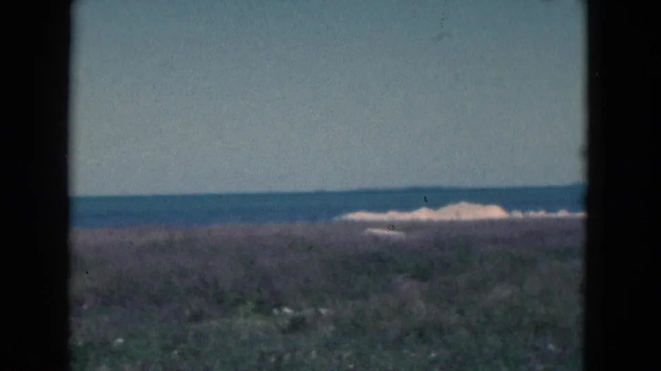 1975 Florida shoreline frame with sea, surf, dune grass, and prominent dark 8mm frame border.