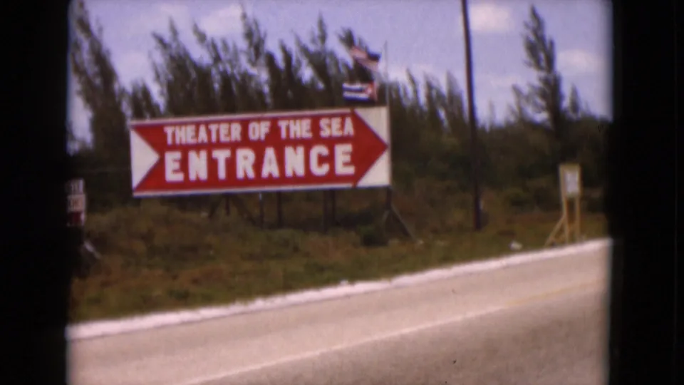 1975 Florida home-movie frame with the Theater of the Sea entrance sign filling much of the roadside view.