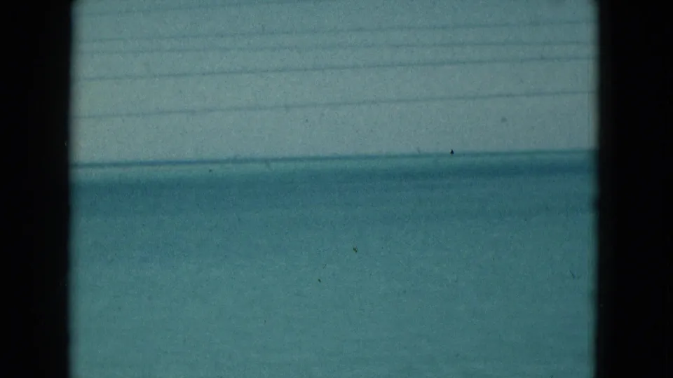 1975 Florida home-movie frame showing blue-green ocean under pale sky, with horizontal lines and dark frame edges visible.