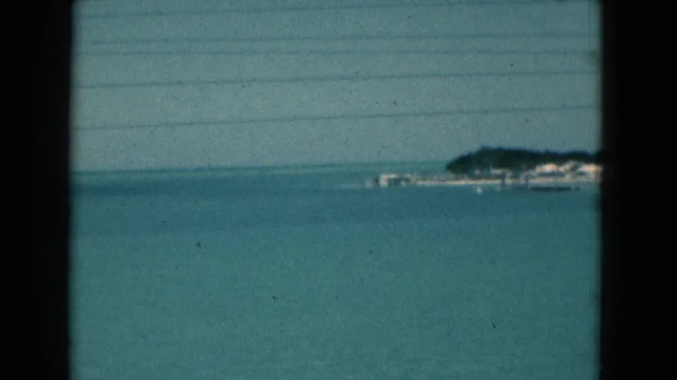 1975 Florida 8mm view of blue ocean with a distant tree-lined shoreline and small coastal structures on the right.