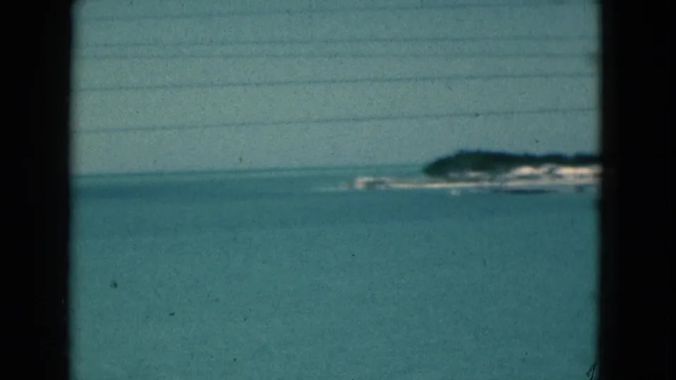 1975 Florida 8mm view of calm coastal water and a distant hazy shoreline, partly framed by dark window-like edges.