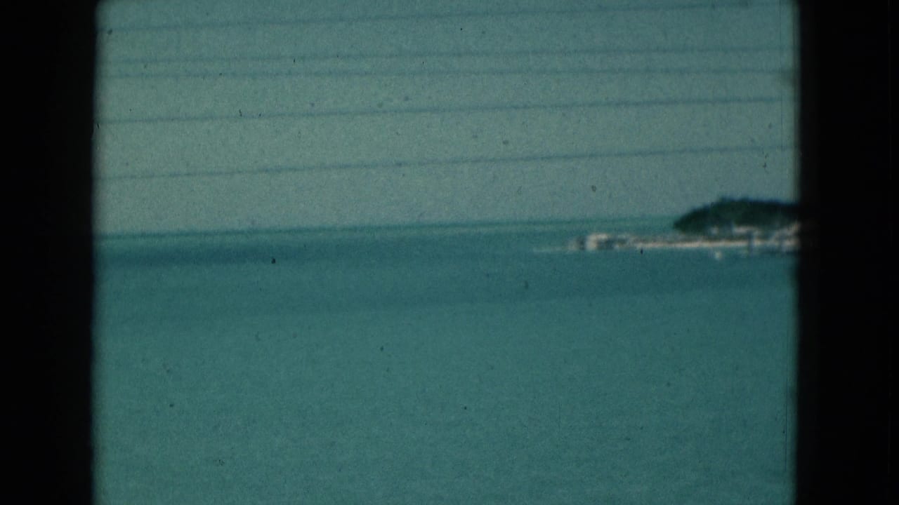 1975 Florida home-movie frame showing open coastal water, distant land, and dark window-like edges crossing the view.