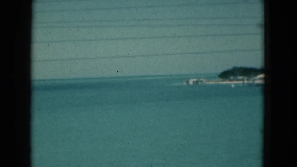 Soft 1975 Florida coastal view with turquoise water, pale horizon, and a low distant shoreline near the edge of the frame.