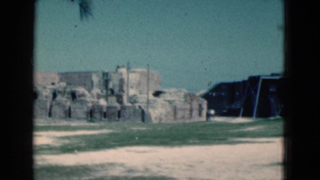 1975 Florida 8mm frame showing weathered stone ruins, pale paths, grass, and a dark bunker-like structure at a coastal sightseeing location.