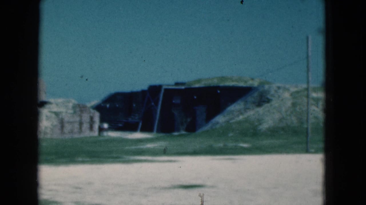 Dark low structure in a grassy sandy landscape with a telephone pole at right.
