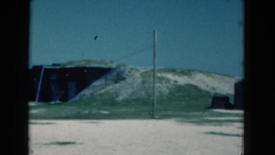 1975 Florida 8mm frame centered on a grassy sandy mound, dark recessed structure, telephone pole, and empty open ground.