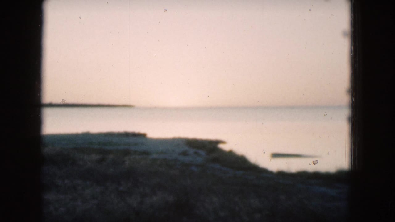 Calm water and dark grassy shoreline seen through an 8mm film frame.