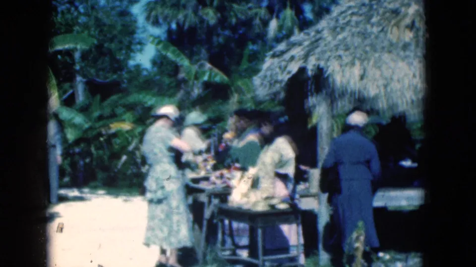 1975 Florida 8mm frame showing visitors near a thatched zoo viewing area surrounded by lush foliage.