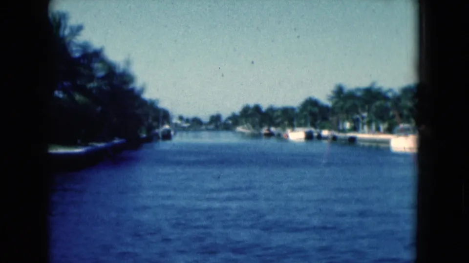 1975 Florida canal view from 8mm footage, with palm-lined banks, distant boats, and waterfront residences.