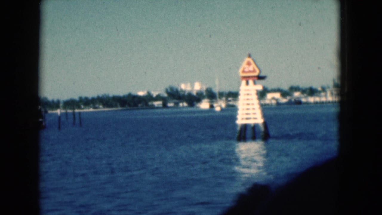 White channel marker on blue water with distant shoreline and dark boat frame edges.