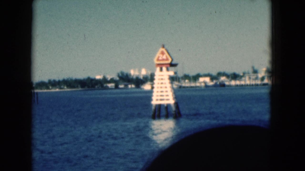 1975 Florida coastal view from a moving boat, with a white channel marker, low shoreline, and dark interior silhouette in the frame.