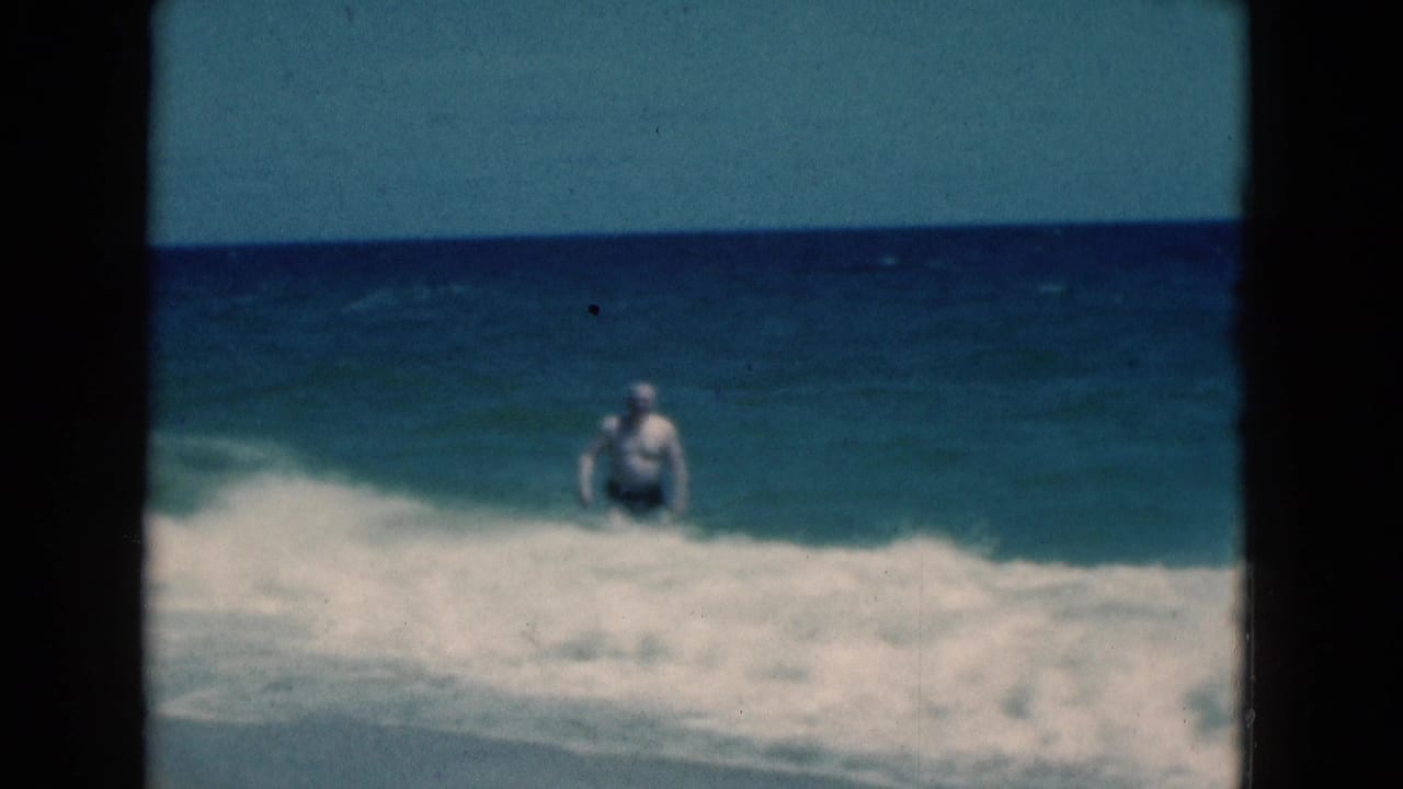 1975 Florida 8mm frame showing a man in a swim cap standing in breaking ocean waves under a blue sky.