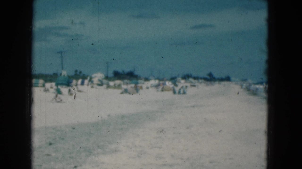 Wide sandy beach with scattered umbrellas and distant beachgoers under a hazy sky.