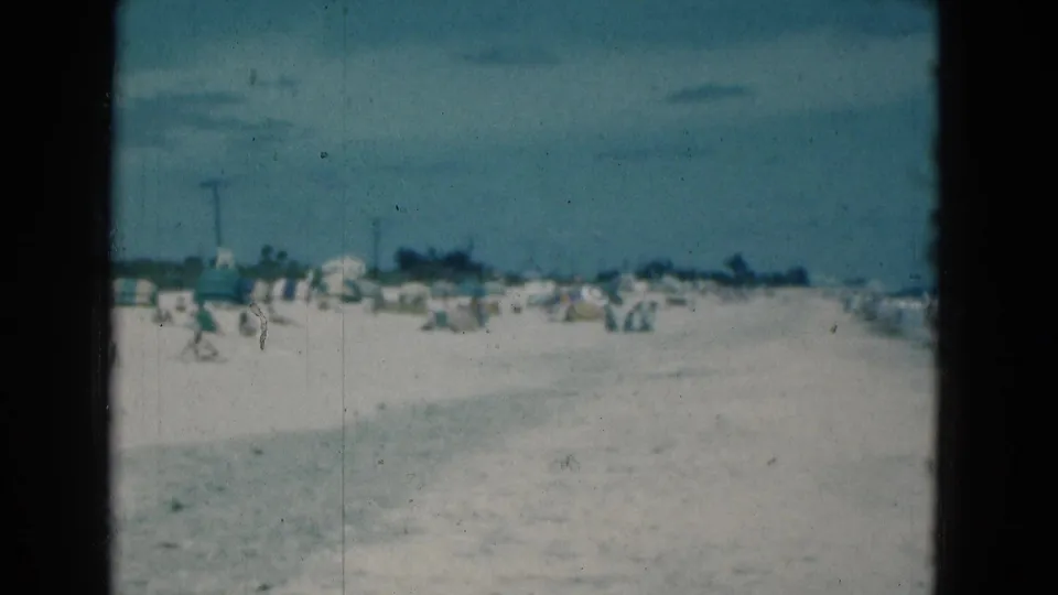1975 Florida 8mm frame showing a wide sandy beach, distant umbrellas, and small figures near the shoreline.