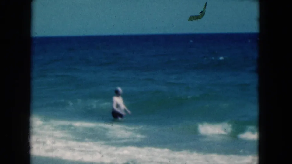 The man continues into the Florida ocean, seen from shore in soft 8mm footage as blue water rises around him.