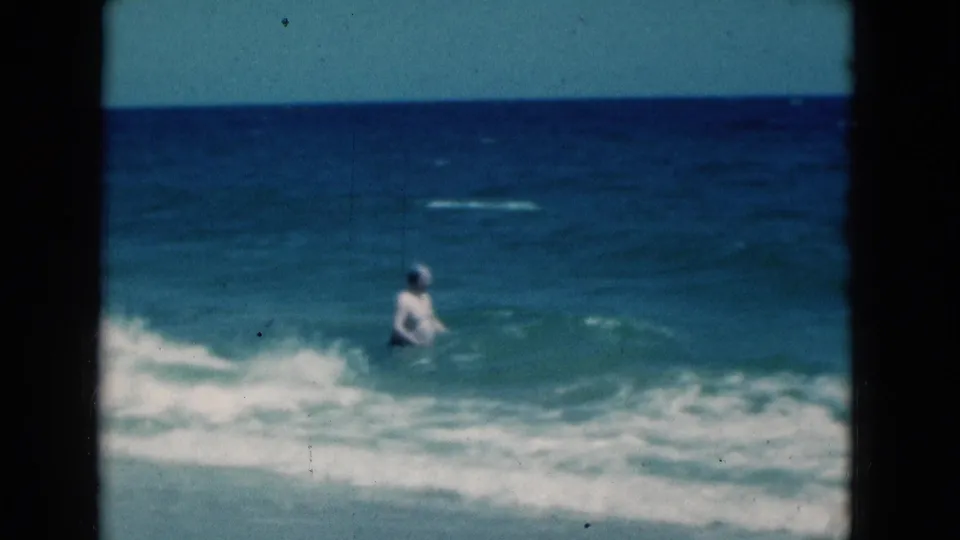 The distant figure appears waist-deep in the Florida surf, with white water crossing the lower frame on 8mm film.