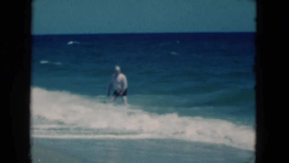 After the wave passes, the man stands in shallow Florida surf with white foam washing toward shore.