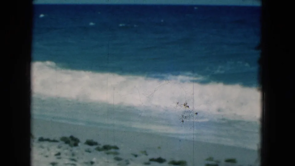 1975 Florida 8mm frame showing blue surf and white foam rolling toward an empty sandy shoreline.