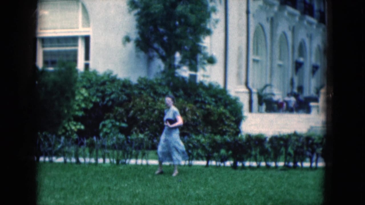 1975 Florida 8mm frame of a woman in a light dress walking on a manicured lawn before a white arched building.