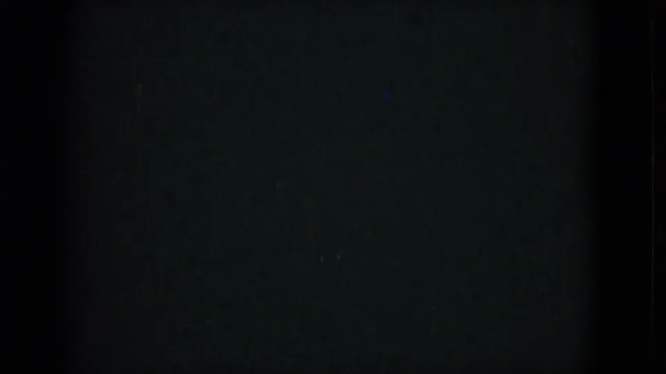 Underexposed 8mm frame with mostly dark field, faint color, and visible film texture between clearer shots.