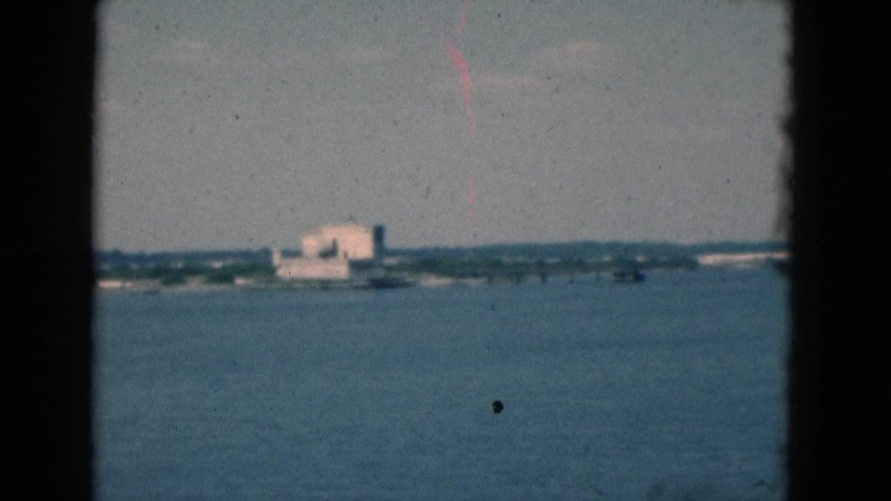 Distant shoreline building across open water, framed by dark film edges.