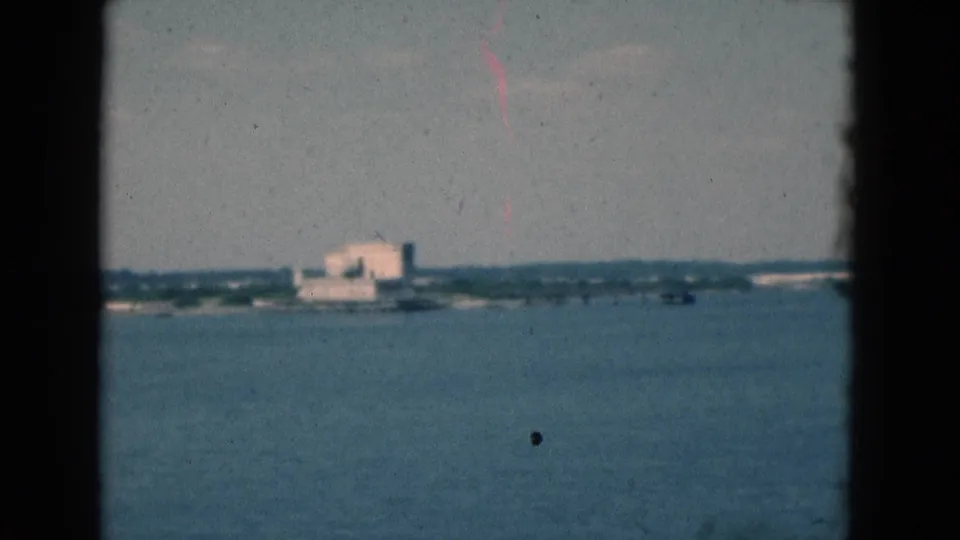 1975 Florida 8mm frame showing open water with a distant shoreline building and dark vertical film borders.