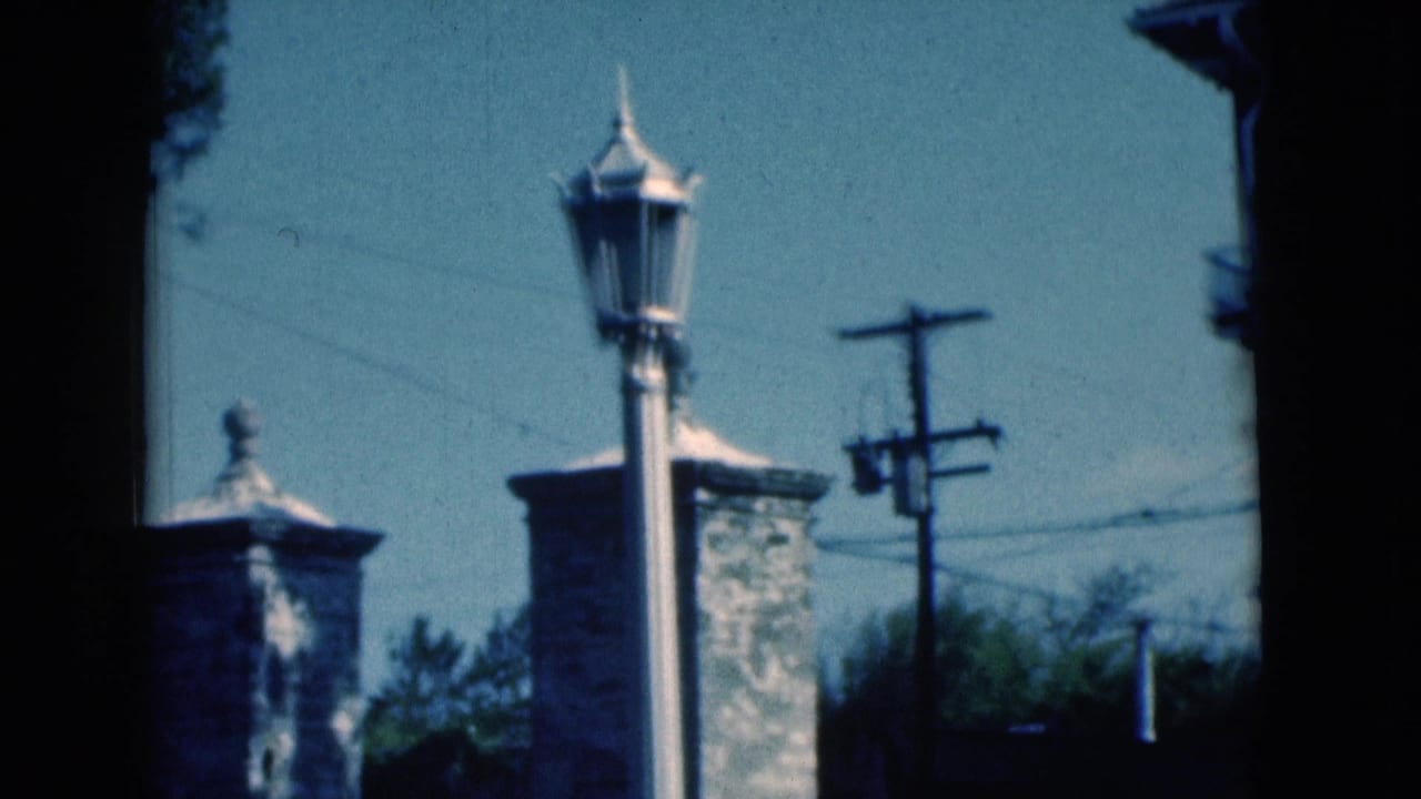 1975 Florida street view with a lamp post foregrounding stone masonry pillars, utility lines, trees, and a low wall.