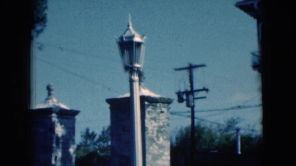 1975 Florida street view with a lamp post foregrounding stone masonry pillars, utility lines, trees, and a low wall.